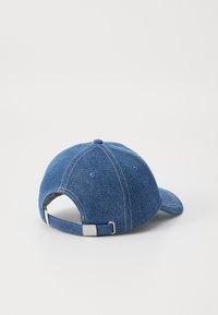 Gorra de denim con visera curvada, correa ajustable en la parte posterior, diseño de seis paneles y costuras blancas en contraste. Color: azul.