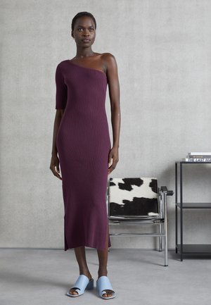 Vestido de malha canelada em bordô com design assimétrico de um ombro, até ao joelho, apresentando fendas laterais. Combinado com sapatos de salto aberto em azul claro.