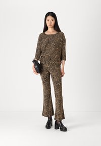 En topp med brun och svart zebramönster samt matchande utsvängda byxor i strukturerad tyg. Modellen håller en svart väska och bär chunky svarta skor.