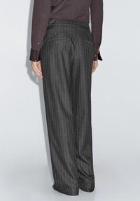 Grijze broek met krijtstreep en een ontspannen pasvorm, voorzien van achterzakken en een gladde tailleband. De stof heeft een subtiele textuur.