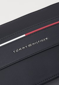 Navy textilná peňaženka s červenými a bielymi horizontálnymi pruhmi, s vyrazeným strieborným logom s nápisom "TOMMY HILFIGER."
