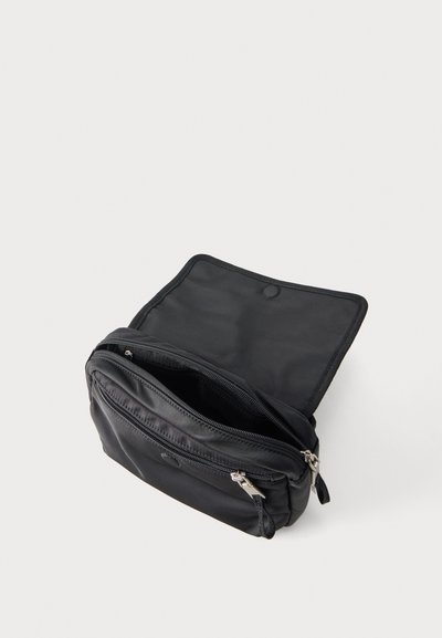 Μαύρη συμπαγής τσάντα ώμου με μπροστινή τσέπη με φερμουάρ και ανοιχτό επάνω καπάκι, που δείχνει το εσωτερικό του κύριου διαμερίσματος, σε απλό φωτεινό φόντο.