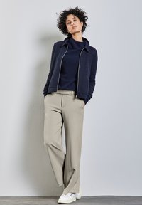 Chaqueta de punto azul marino sobre una camiseta azul marino, combinada con pantalones de pierna ancha beige y zapatillas blancas. Tejido texturizado con un diseño estructurado.