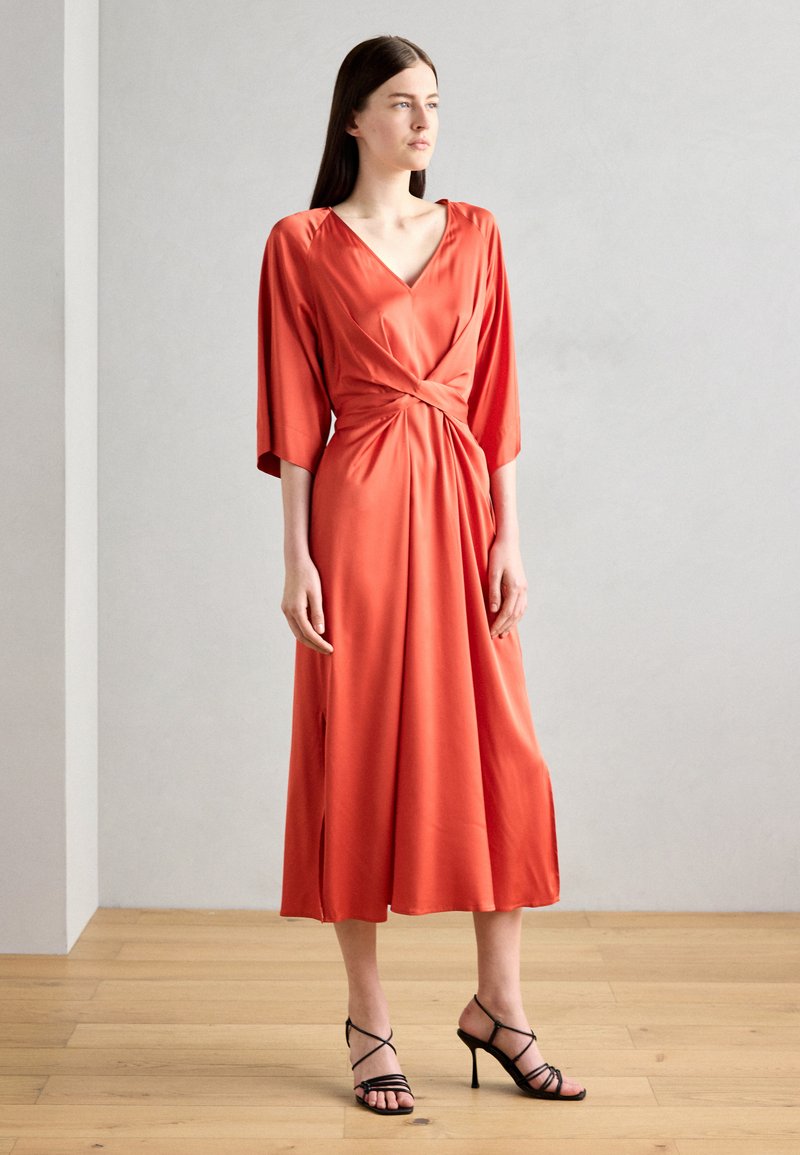 Rochie din satin, de culoare portocalie vibrantă, cu decolteu în V, mâneci trei sferturi, detaliu pliat la talie și o lungime până la genunchi cu fante.
