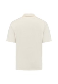 Korte mouw polo in gebroken wit, met een gestructureerde brei-stof. Heeft een klassieke kraag en een strakke, minimalistische uitstraling met een ontspannen pasvorm.
