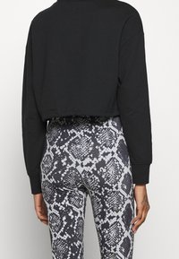 Felpa nera a maniche lunghe e cropped abbinata a leggings stampati in bianco e nero con motivo a serpente e una finitura testurizzata.