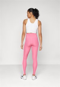 Witte sportieve crop top gecombineerd met hoge, roze leggings met witte zijstrepen, een gladde textuur en een aansluitend ontwerp.