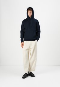 Navy hooded sweatshirt with a front pocket, paired with cream wide-leg trousers and black loafers. Simple design, cotton blend material.