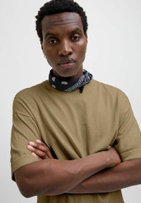 Tan kortærmet T-shirt med rund hals, der har en glat overflade. Båret med et sort bandana om halsen, mønstret med hvide accenter.