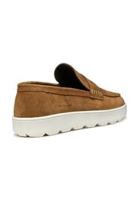 Scarpa slip-on in suede marrone con punta tonda e suola in gomma bianca caratterizzata da una superficie testurizzata. I dettagli includono cuciture lungo la parte superiore.