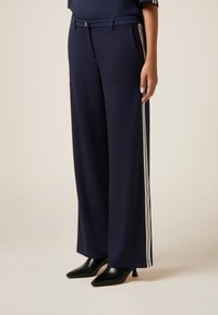 Pantaloni palazzo blu navy realizzati in tessuto morbido, con una striscia laterale a contrasto, due tasche frontali e una cintura. Abbinati a tacchi neri a punta.