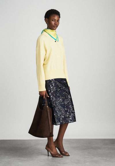 Pull en maille jaune avec un col montant, jupe à sequins florale navy, sac à main en suede marron et sandales ouvertes marron.