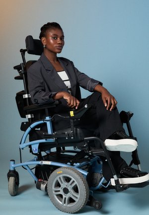 Silla de ruedas eléctrica con un marco azul, asiento negro y ruedas grises. El usuario lleva un blazer gris y pantalones negros, sentado con confianza.