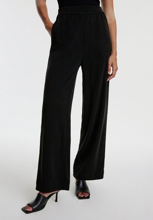 Zwarte wijde broek met een gestructureerde stof, voorzien van een elastische tailleband en zijzakken, gecombineerd met open-toed zwarte hakken.