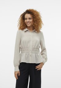 Lys beige knappestykke skjorte med teksturert stoff, samling i midjen, lange ermer og klassisk krage.