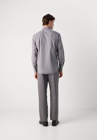 Camicia grigia a maniche lunghe e pantaloni coordinati realizzati in tessuto liscio. La camicia presenta un colletto a punta e polsini con bottoni, abbinata a calzature nere.