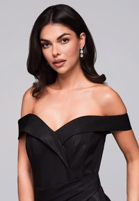 Černá off-shoulder večerní šaty mají strukturovaný design s saténovou texturou a úhlovými sklady. Doplňuje je zavěšené náušnice. Hladký, elegantní silueta.
