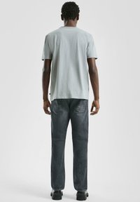 Jasnoszara bawełniana koszulka z krótkimi rękawami, zestawiona z ciemnymi dżinsami. Dżinsy mają klasyczny styl z pięcioma kieszeniami i delikatną fakturę.