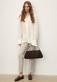 Chemise blanche à manches longues avec boutons, pantalon beige sur mesure, mocassins marron et sac à main marron foncé. Tissus lisses et design simple.