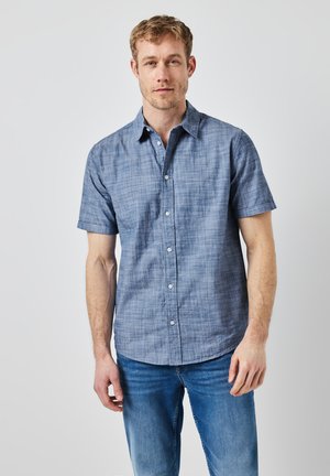 Camisa de manga corta de botones hecha de una ligera tela a cuadros azul, con cuello, frente con botones y un corte relajado, combinada con jeans.