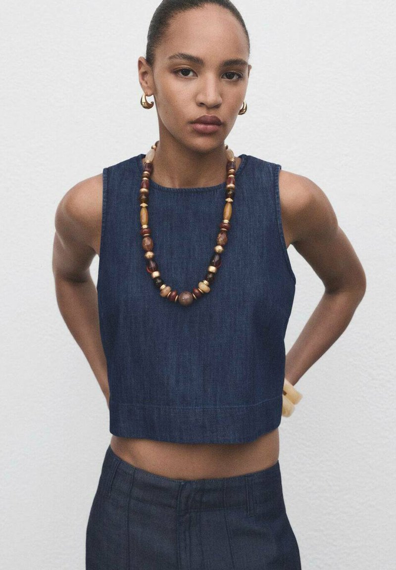 Denim crop top met een ronde halslijn, voorzien van een mouwloos ontwerp. Vergezeld van een ketting met gekleurde kralen en een armband van natuurlijk hout.