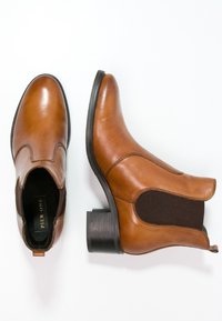 Stivaletti in pelle marrone con punta rotonda, pannelli laterali elasticizzati e tacco a blocco basso. Texture liscia con dettagli di cucitura sottili.