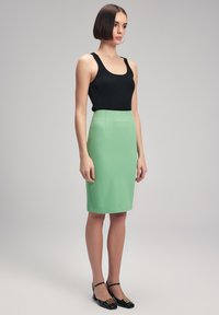 Débardeur noir à côtes associé à une jupe fitted vert menthe de longueur genou. Le mannequin porte des chaussures noires avec des accents décoratifs.