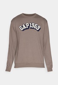 Sweatshirt marron à manches longues avec des poignets et un ourlet côtelés. Présente un logo brodé "GAP 1969" en bleu marine et blanc sur la poitrine.