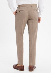Hellbraune Hose aus strukturiertem Stoff mit Karomuster, ausgestattet mit zwei Gesäßtaschen und getragen mit braunen Schuhen.