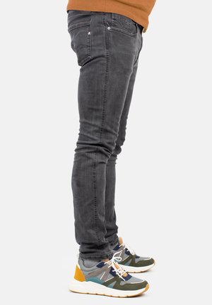 Jeans ajustados gris con detalles de costura visibles, combinados con zapatillas multicolores con acentos de malla y goma.