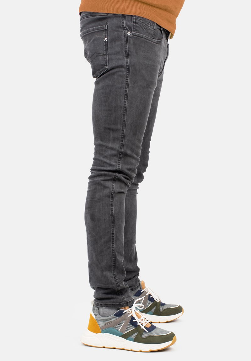 Jeans ajustados gris con detalles de costura visibles, combinados con zapatillas multicolores con acentos de malla y goma.