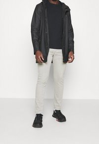 Svart vattentålig jacka med huva, svart t-shirt, ljusgrå slim-fit jeans och svarta träningsskor med rosa detaljer.