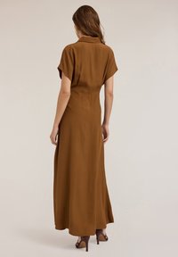 Brown maxi dress with short sleeves, collared neckline, flowing design, smooth texture, and a straight cut to the floor, paired with heeled shoes.