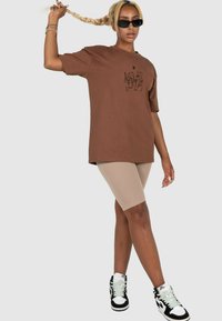 Brun oversized t-shirt med logo print, beige cykelshorts og sort-hvide højtop sneakers. Glat materiale, afslappet pasform.