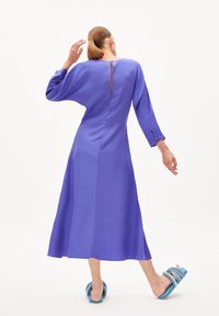 Vestito viola a maniche lunghe con scollatura rotonda e dettaglio a chiave sulla schiena. Accompagnato da sandali blu con fasce larghe. Tessuto liscio.