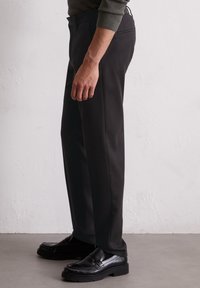 Pantaloni neri su misura realizzati in tessuto morbido, con un design a gamba dritta e una tasca posteriore, abbinati a mocassini neri lucidi.