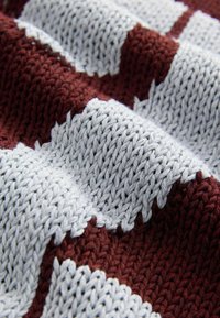 Stickad textil med växlande vinröda och grå sektioner med ett strukturerat mönster. Tyget har en mjuk, taktil kvalitet.