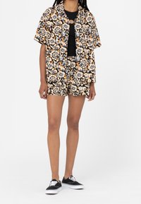 Ensemble chemise et short à imprimé floral en noir, orange et crème. Coupe ample, manches courtes, et short assorti avec un motif similaire.
