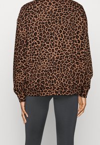 Luipaardprint sweatshirt in bruin en zwart, met een relaxte pasvorm, geribbelde manchetten en een gebogen zoom. Gecombineerd met strakke grijze leggings.