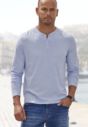 Hellblaues Langarm-Henley-Shirt mit zwei Knöpfen am Ausschnitt, kombiniert mit blauen Jeans aus Denim. Texturiertes Material, lockere Passform.