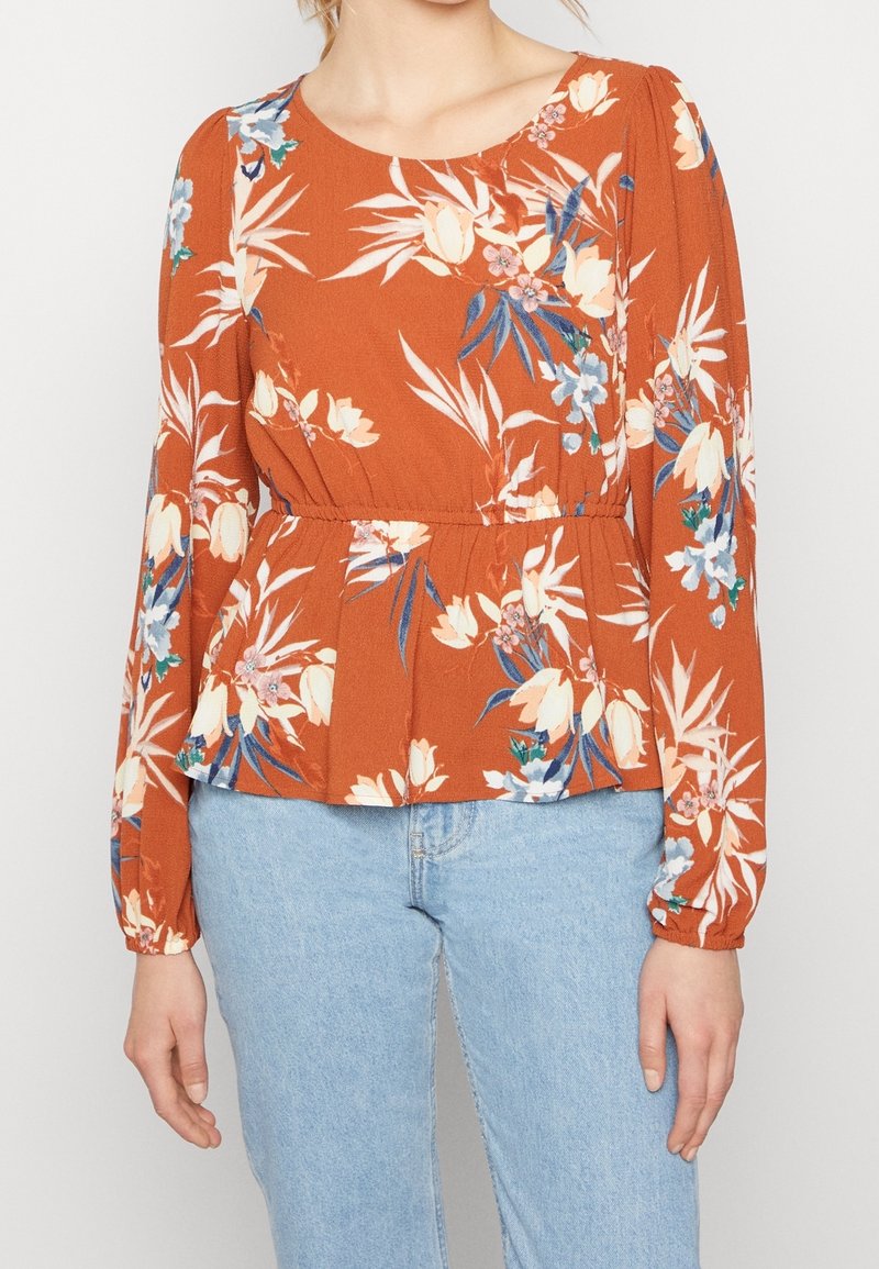 Rostfarbige Bluse mit langen Ärmeln, mit einem Peplum-Taille, runder Halslinie und lebhaften blauen und cremigen Blumenmustern.