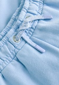 Gaiši zili kokvilnas sporta bikses ar elastīgu jostu un mežģīnēm, pabeigtas ar sudraba acīm un platas virves auklām.