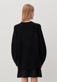 Oversized black sweater with a textured, soft fabric, round neckline, and raglan sleeves. Ribbed hem and cuffs for added detail.