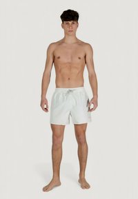 Beli plavalni kratke hlače iz lahkega materiala, z elastičnim pasom z vrvico, stranskimi žepi in sproščenim krojem.