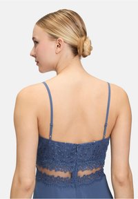 Robe bleue avec des bretelles spaghetti et un panneau arrière en dentelle et sequins. Le tissu a une texture lisse et une silhouette ajustée.