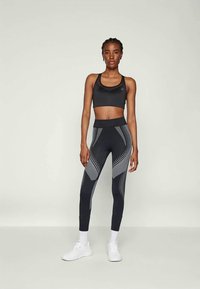Reggiseno sportivo nero e leggings a vita alta con motivi geometrici grigi e dettagli riflettenti, abbinati a scarpe da ginnastica bianche.