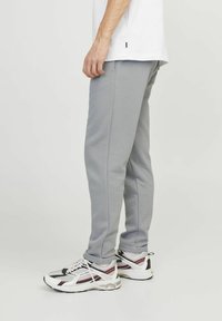 Light grey sweatpants made of soft fabric, featuring a tapered fit and side pockets, paired with white sneakers with black and red accents.