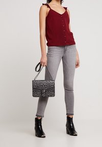 Burgundowa bezrękawnik z falbanastymi ramiączkami i detalem z guzikami, szare skinny jeans, czarne botki za kostkę oraz torebka w czarny teksturowany wzór węża.
