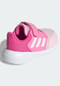Różowy but sportowy z cholewką z siateczki, syntetycznymi akcentami, paskiem na rzep oraz białym logo z trzema paskami; fakturowana gumowa podeszwa.