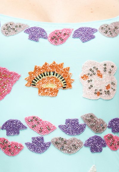 Lyseblåt stof dekoreret med farverige perlebesatte blomster- og vifteformede mønstre i orange, pink, lilla og sølvtoner.